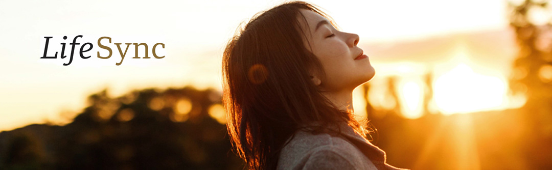 A young woman from the shoulders up, eyes closed, looking to the right and upward. Sun rising or setting in the background